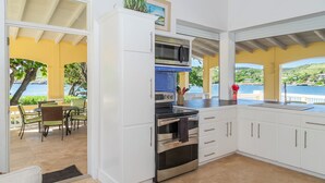 A kitchen with white cabinets, a stainless steel oven, and a microwave. There is a view of the sea through large windows. - Wake up in paradise at this amazing villa for couples and families (St.Paul)