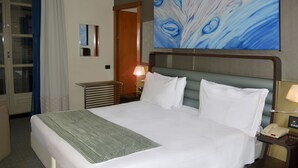 Habitación de hotel con una cama grande, una mesita de noche con lámpara, teléfono y un cuadro en la pared.