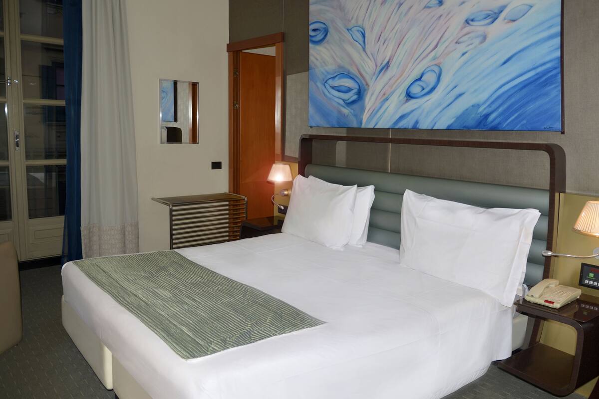Habitación de hotel con una cama grande, una mesita de noche con lámpara, teléfono y un cuadro en la pared.
