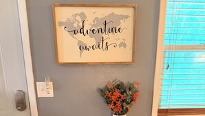 Ein gerahmtes Schild mit Text, ein gewebter Korb, eine Vase mit Blumen und ein kleiner Tisch an einer Wand.