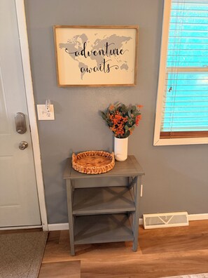 A framed sign with text, a woven basket, a vase with flowers, and a small table against a wall. - Great location duplex (Stevens Point)