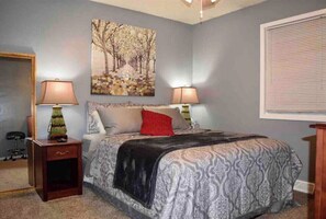 A bedroom with a bed, two bedside lamps, a nightstand, a mirror, and a painting on the wall. - Great location duplex (Stevens Point)