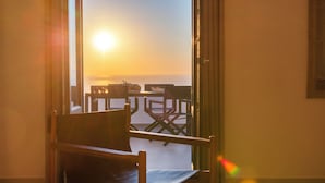 A room with a wooden chair and a table, a view of the sunset, and a balcony with chairs and a table. - La Maltese Villas Santorini (Santorini)