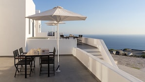 A terrace with a table and chairs, a white umbrella, and a view of the sea. - La Maltese Villas Santorini (Santorini)