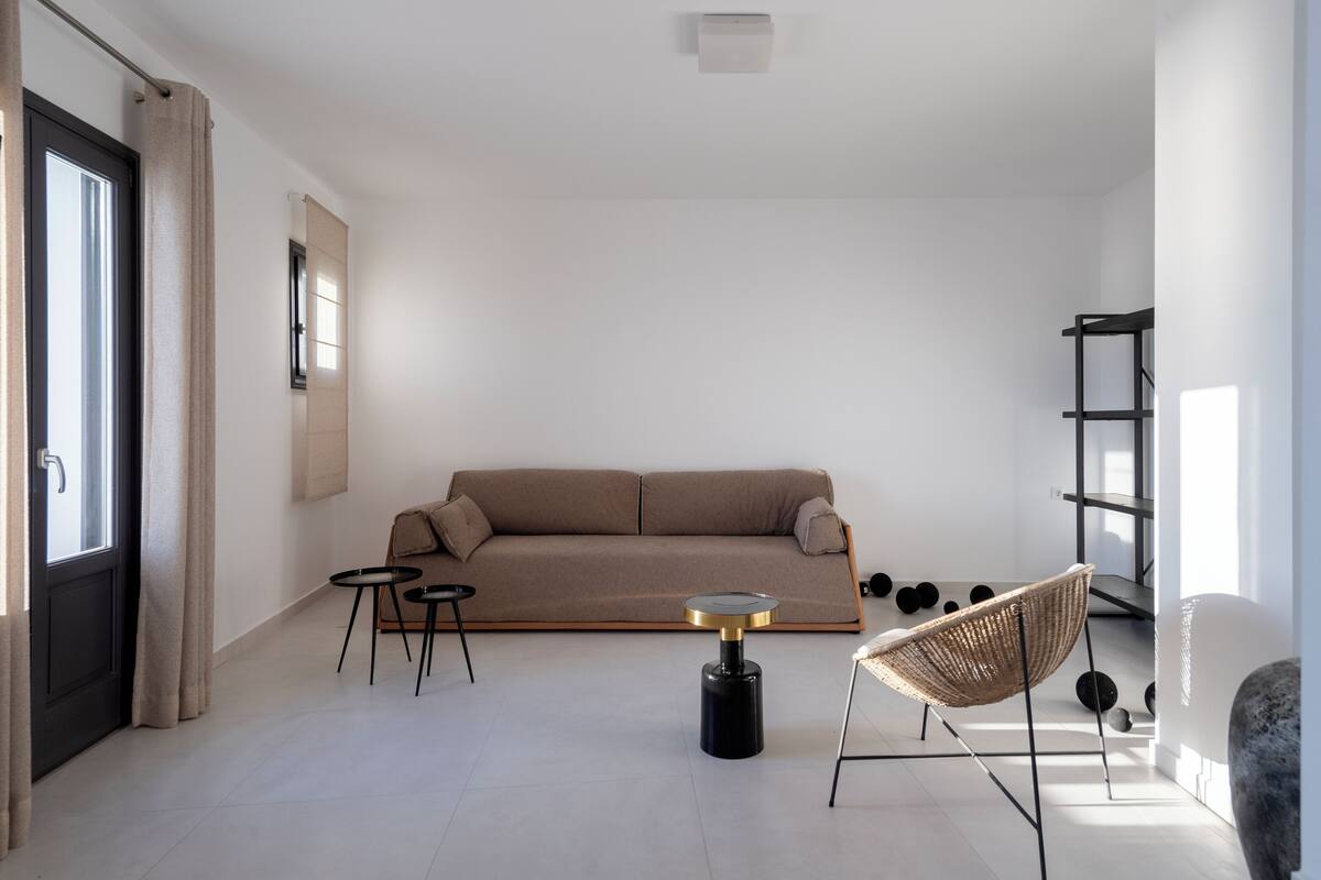 Ein minimalistisch eingerichtetes Wohnzimmer mit einer Couch, zwei kleinen Tischen, einer Stehlampe und einem Korbstuhl.