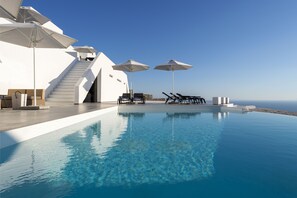 Una piscina infinita con agua azul cristalina, arquitectura blanca y mobiliario exterior con sombrillas.