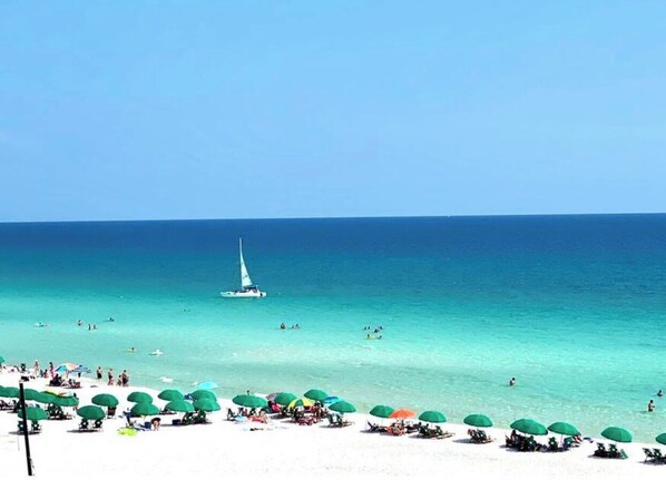 Guests can enjoy the beach with umbrellas providing shade and a sailboat visible in the distance.
