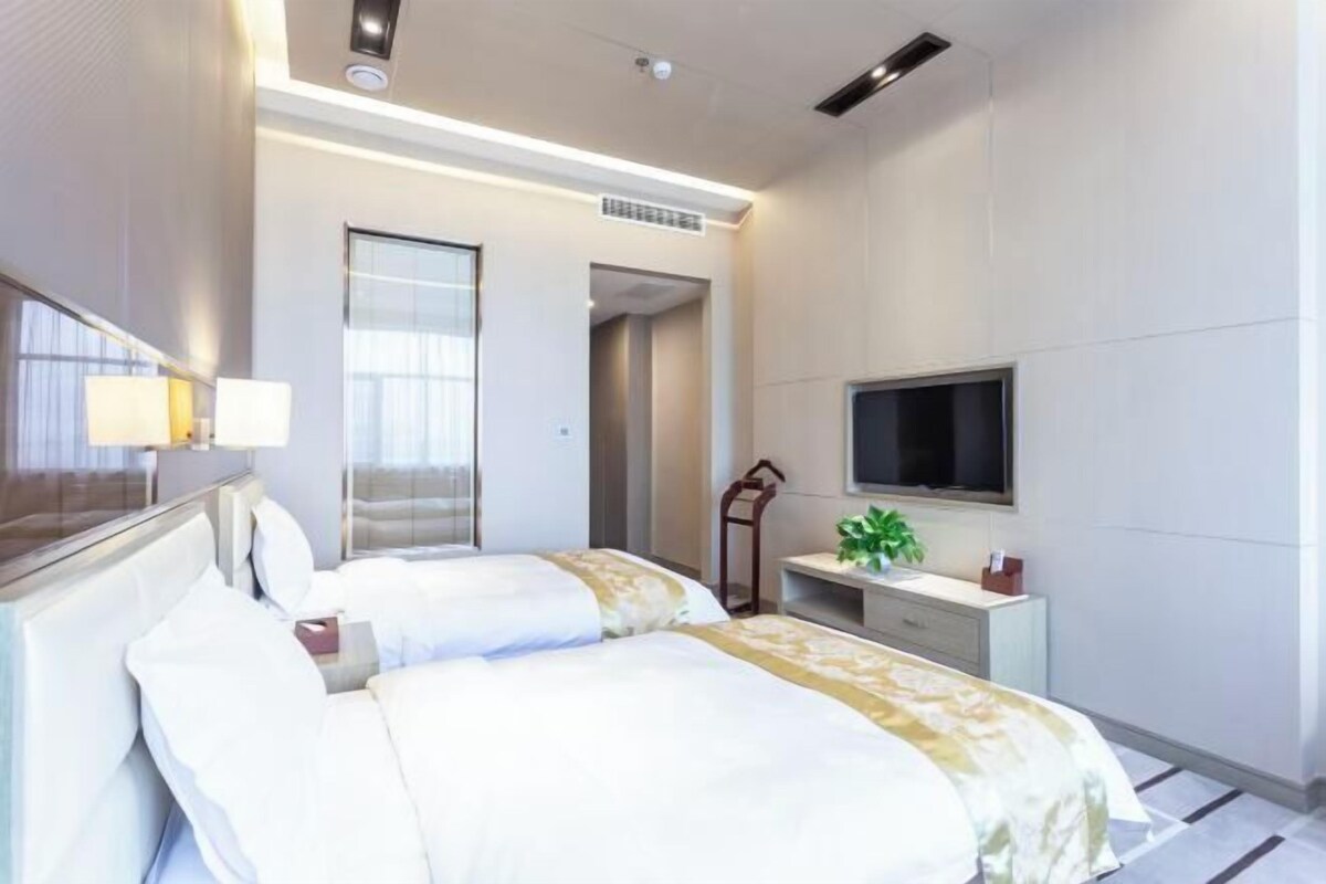 A hotel room with two beds, a TV, a desk, and a mirror.