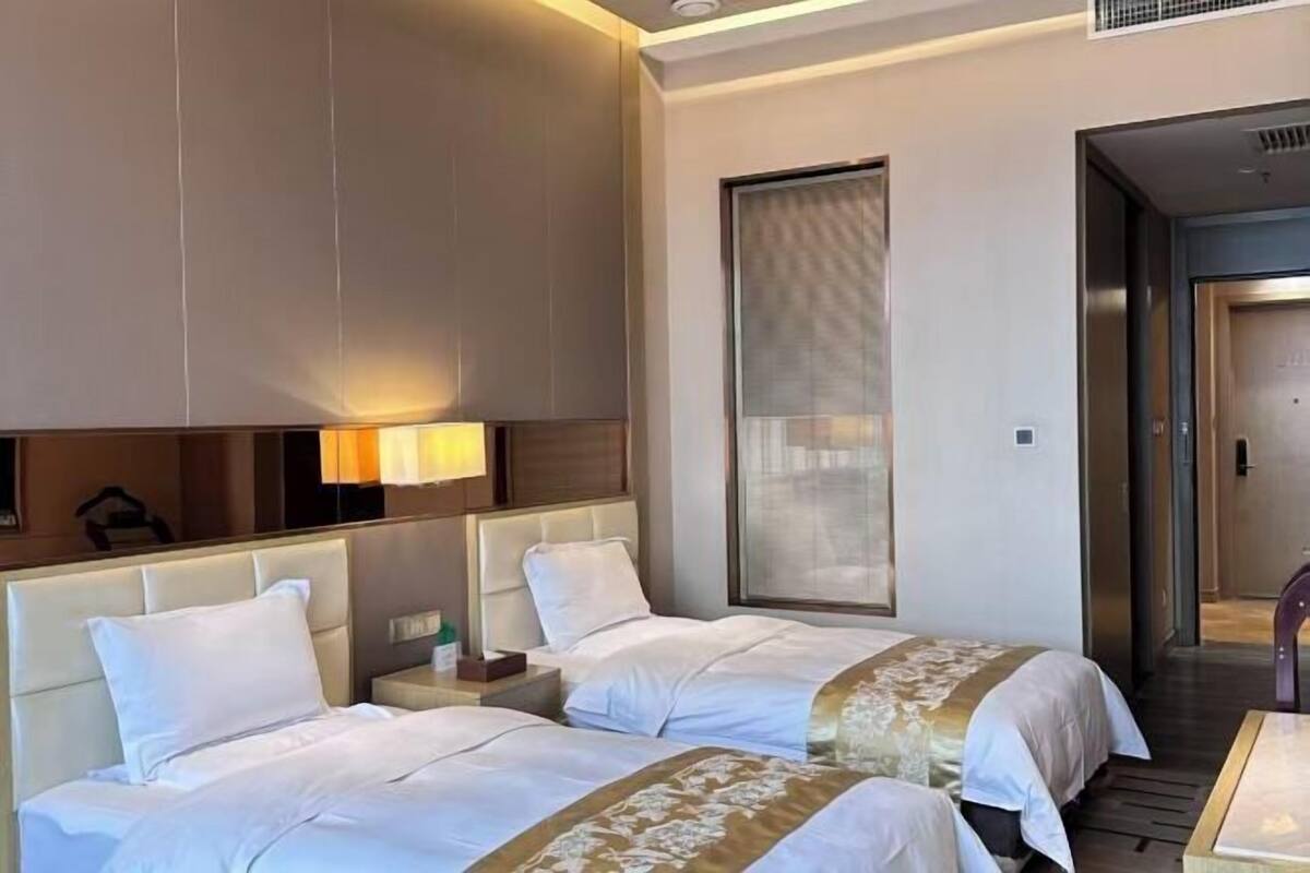 A hotel room with two beds, a large mirror, a nightstand, and a window with blinds.