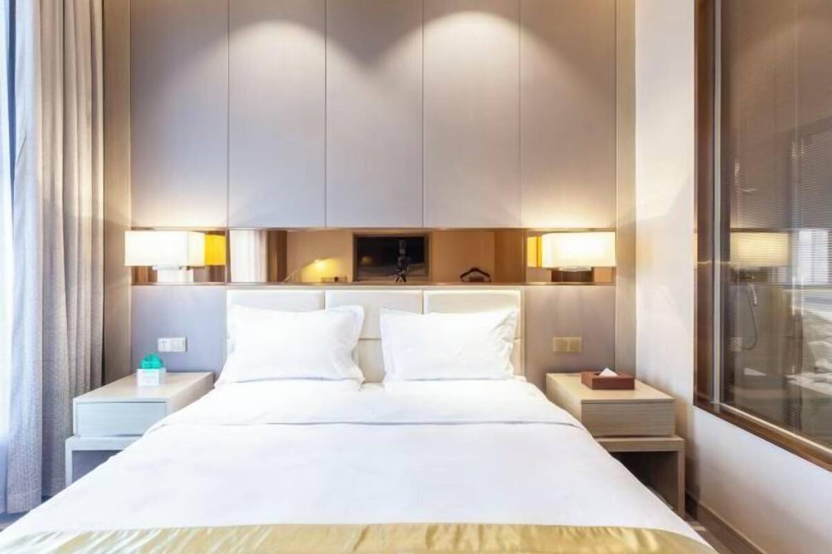 A hotel room with a large bed, two bedside tables, a nightstand, and a window with blinds.
