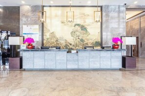 A reception desk with a marble floor, two lamps, and a painting in the background. - Fengze Business Hotel (Fanshi)