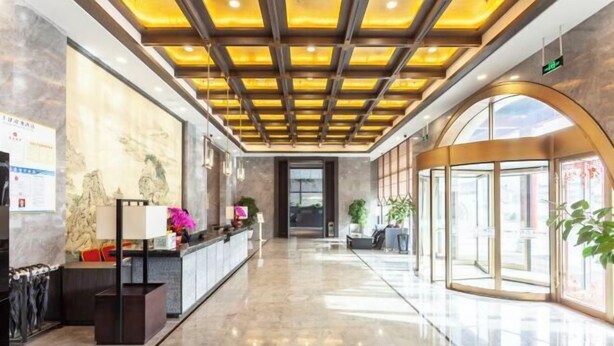 Un vestíbulo de hotel moderno con suelo de mármol, una recepción, un cuadro grande en la pared y una entrada de vidrio.