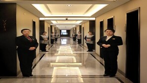 Pasillo de hotel con piso reflectante, puertas a ambos lados e iluminación uniforme.