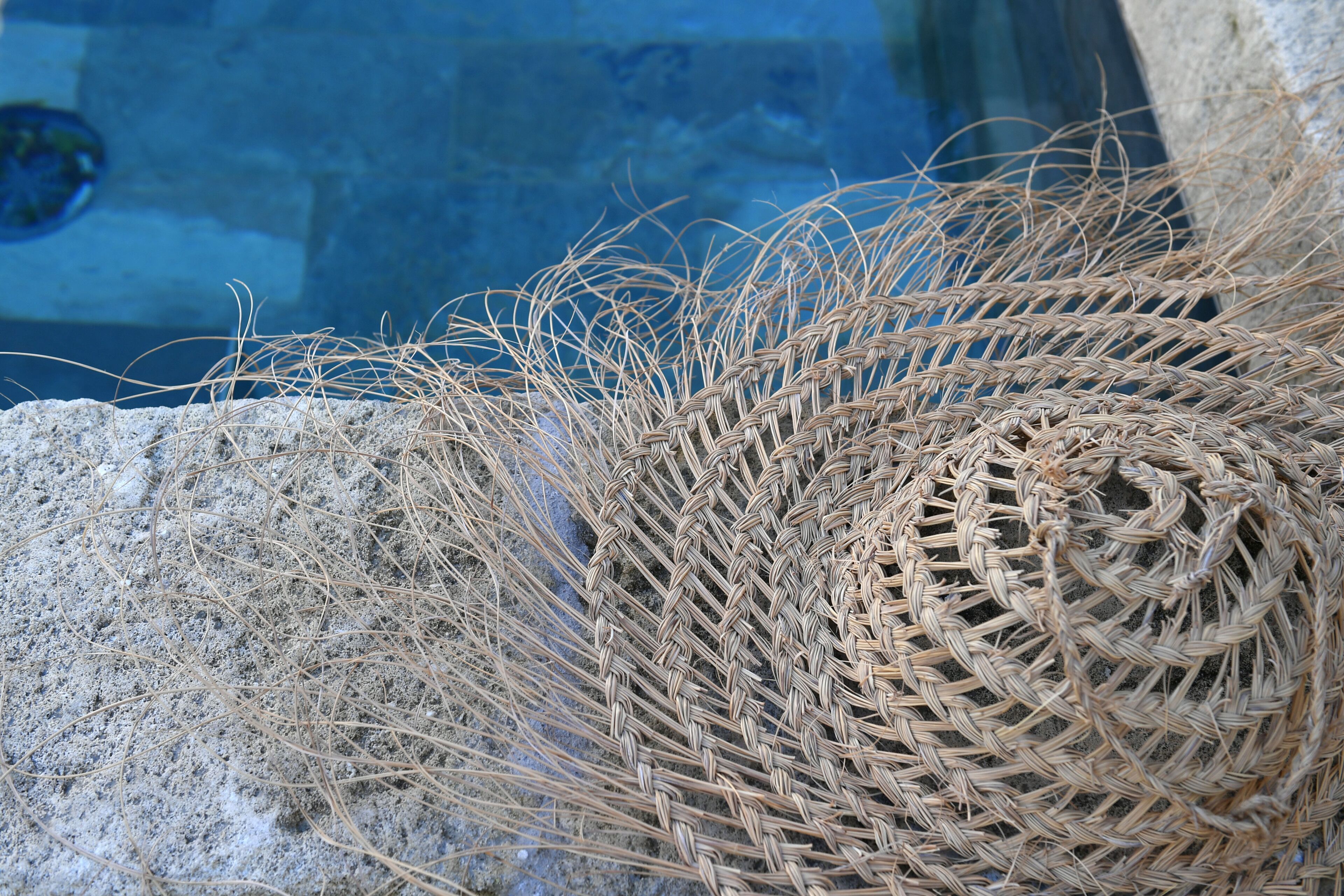 Un gros plan d’un panier tressé orné d’un motif en spirale, posé sur une surface en pierre, près d’une piscine.