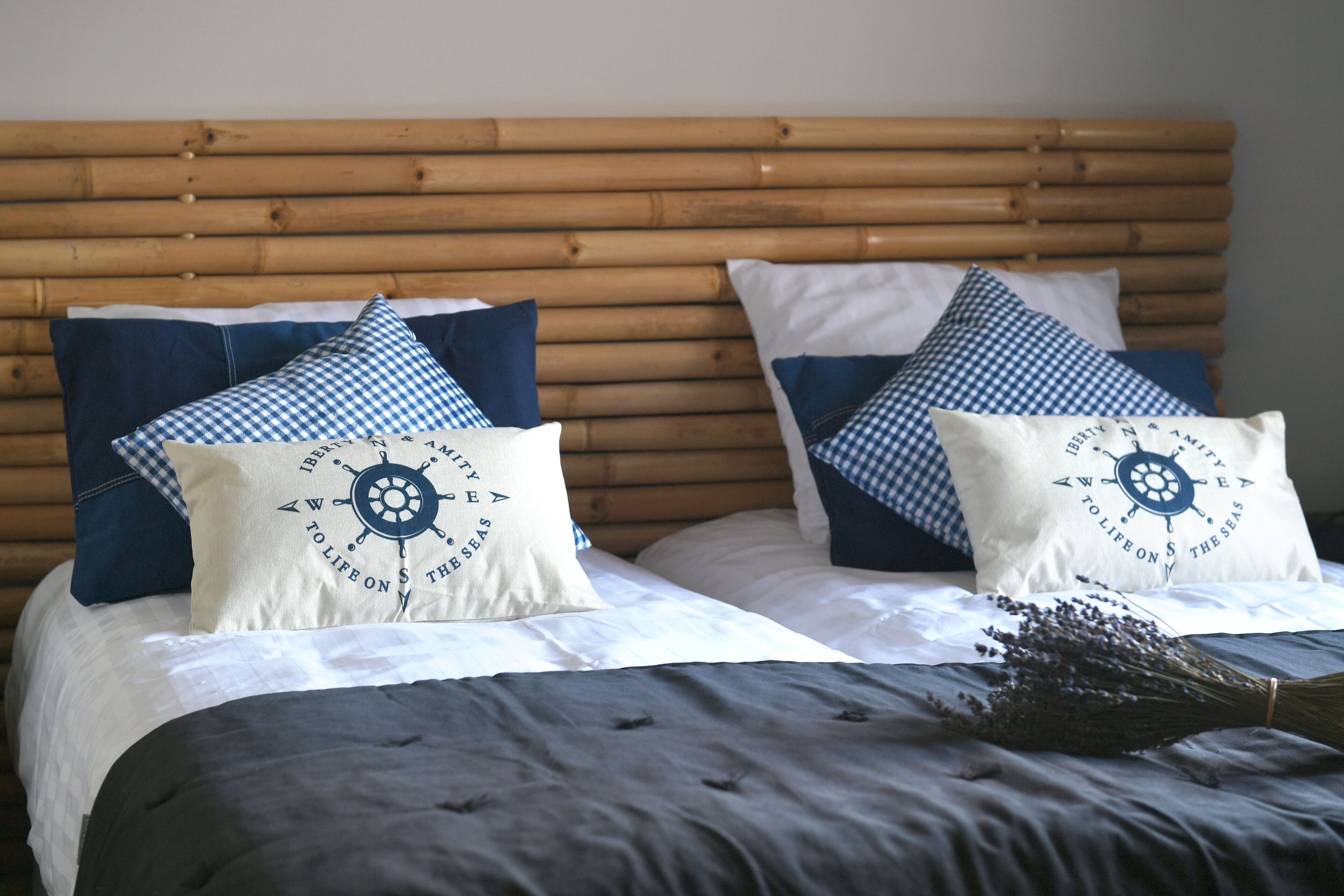 Un lit avec une tête de lit en bois, deux oreillers ornés de motifs marins et une couvre-lit gris foncé.