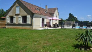 Una casa con techo inclinado, un patio con mobiliario exterior y una piscina al fondo.