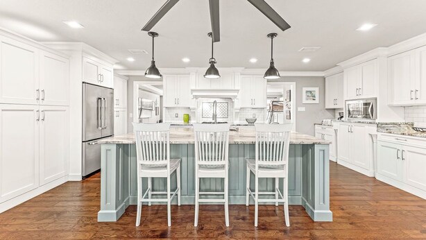 A spacious kitchen with white cabinetry, a central island with bar stools, and a ceiling fan.