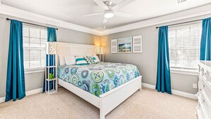 A bedroom with a bed, a ceiling fan, and two windows with curtains.
