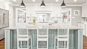 A kitchen with white cabinets, a marble countertop, and three white bar stools.