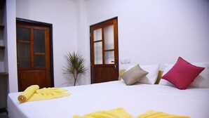 Ein Hotelzimmer mit einem ordentlich bezogenem Bett, einer Zimmerpflanze und zwei Holztüren.