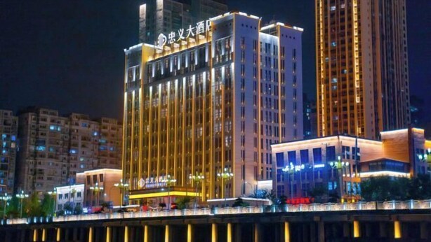 Um hotel com vários andares, sinalização iluminada, entrada destacada e vista para o rio.