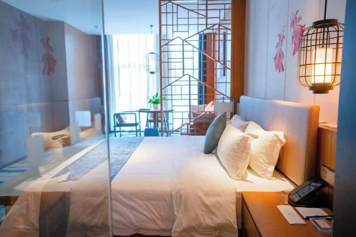 Habitación de hotel con cama, escritorio, silla, escalera y pared decorada con obras de arte.