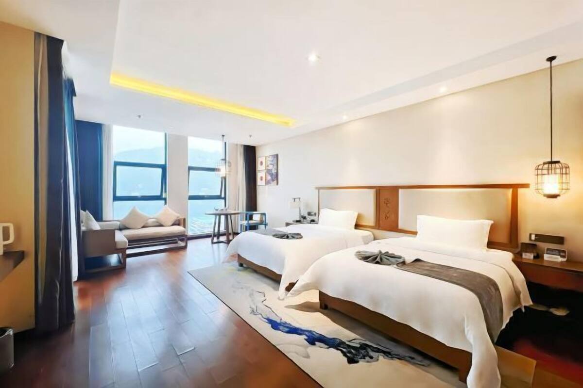 Habitación de hotel con dos camas, un sofá, una mesita y vistas al exterior.