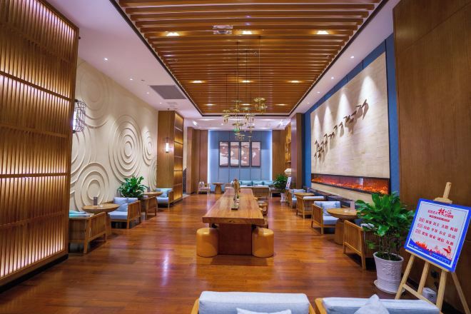 A hotel lobby with a central dining table, seating arrangements, and a reception desk.