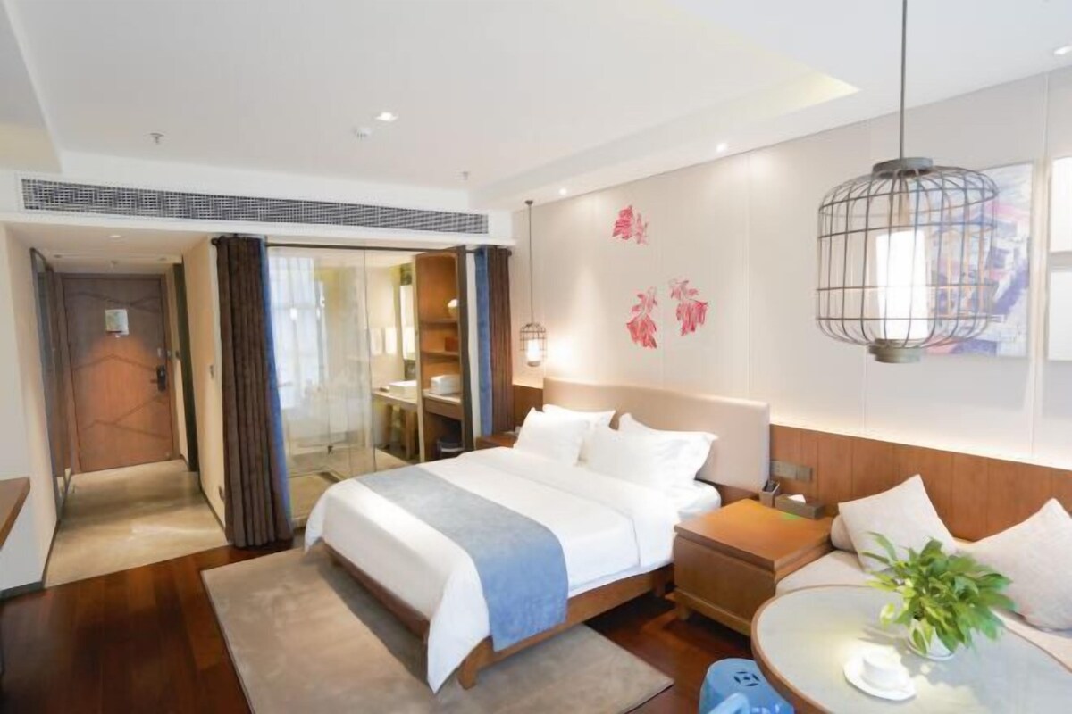 Habitación de hotel moderna con una cama grande, mesitas de noche, una mesa de centro redonda y vistas de la ciudad a través de la ventana.