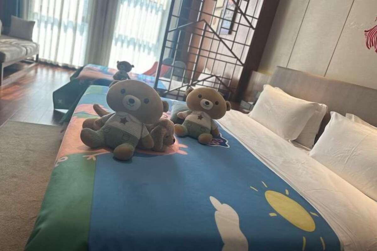 A hotel room with a bed, a sofa, and two teddy bears on the bed.