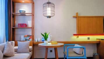 A cozy room with a sofa, a small table with a plant, a blue chair, a wooden shelf with items, and a hanging light fixture.