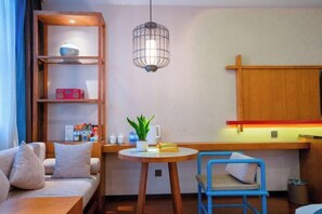 A cozy room with a sofa, a small table with a plant, a blue chair, a wooden shelf with items, and a hanging light fixture. - Zhongyi Hotel (Zhong County)
