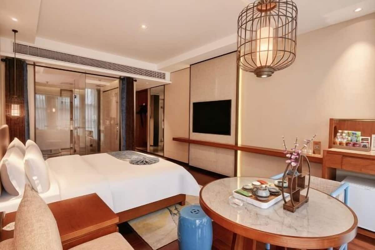 Una habitación de hotel moderna con cama, una mesa redonda de comedor con juego de té, un televisor y una lámpara decorativa.