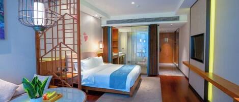 A modern hotel room with a bed, a dining area with a table and chairs, a TV, and a decorative wooden partition.