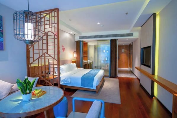 A modern hotel room with a bed, a dining area with a table and chairs, a TV, and a decorative wooden partition. - Zhongyi Hotel (Zhong County)