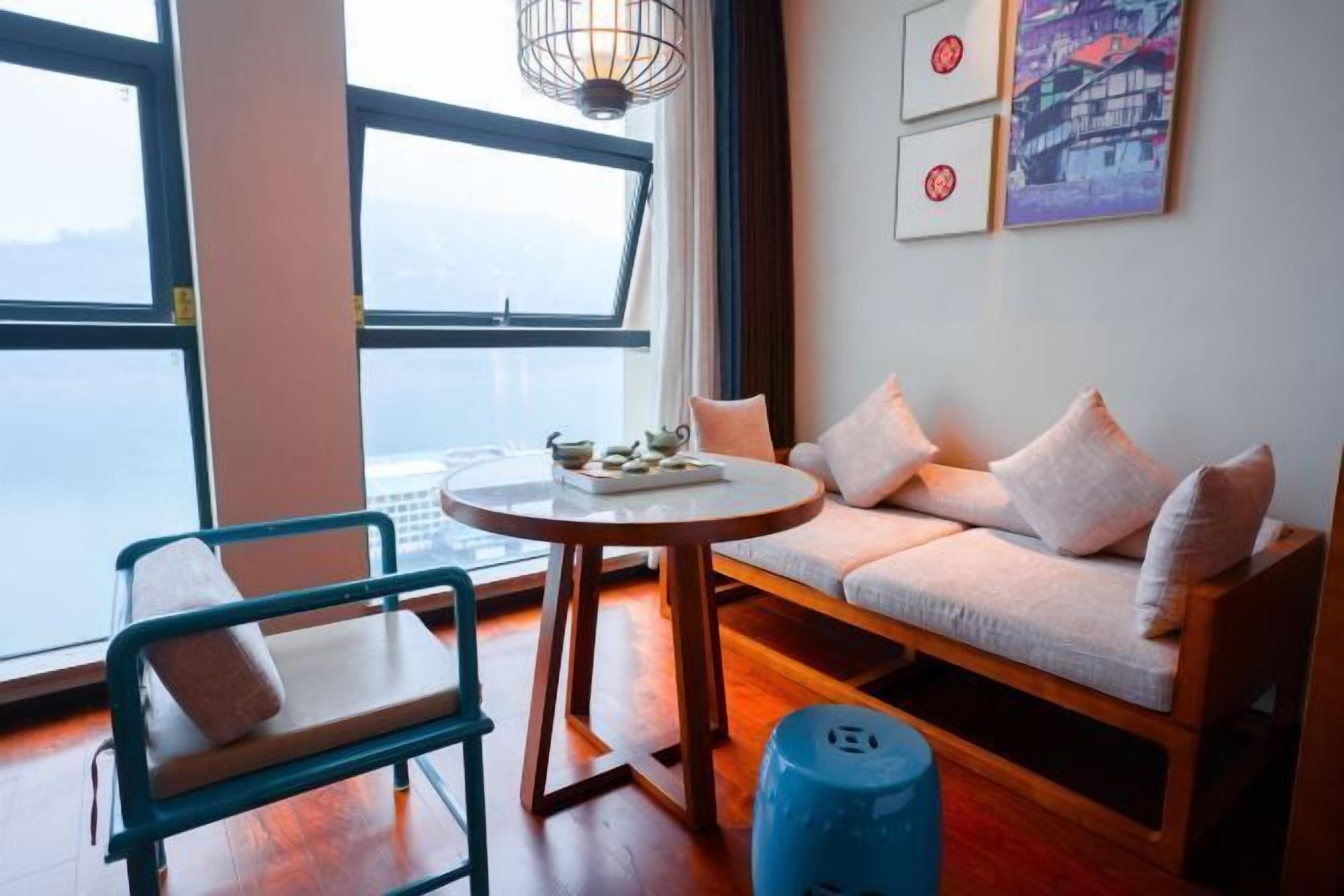 A room with a sofa, a chair, a round table, and a view of the sea.