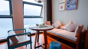 A room with a sofa, a chair, a round table, and a view of the sea.