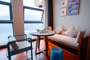 A room with a sofa, a chair, a round table, and a view of the sea.
