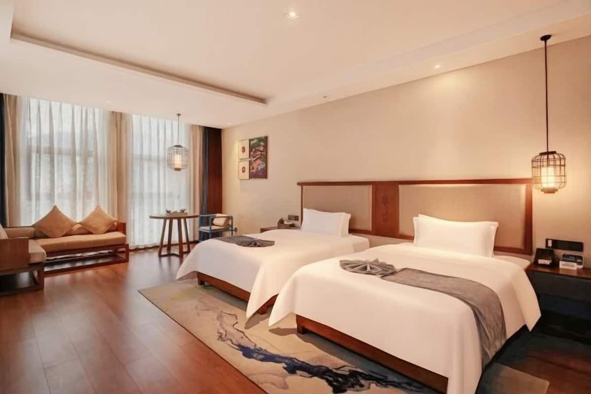 Habitación de hotel con dos camas, un sofá, una mesita y vistas al exterior.