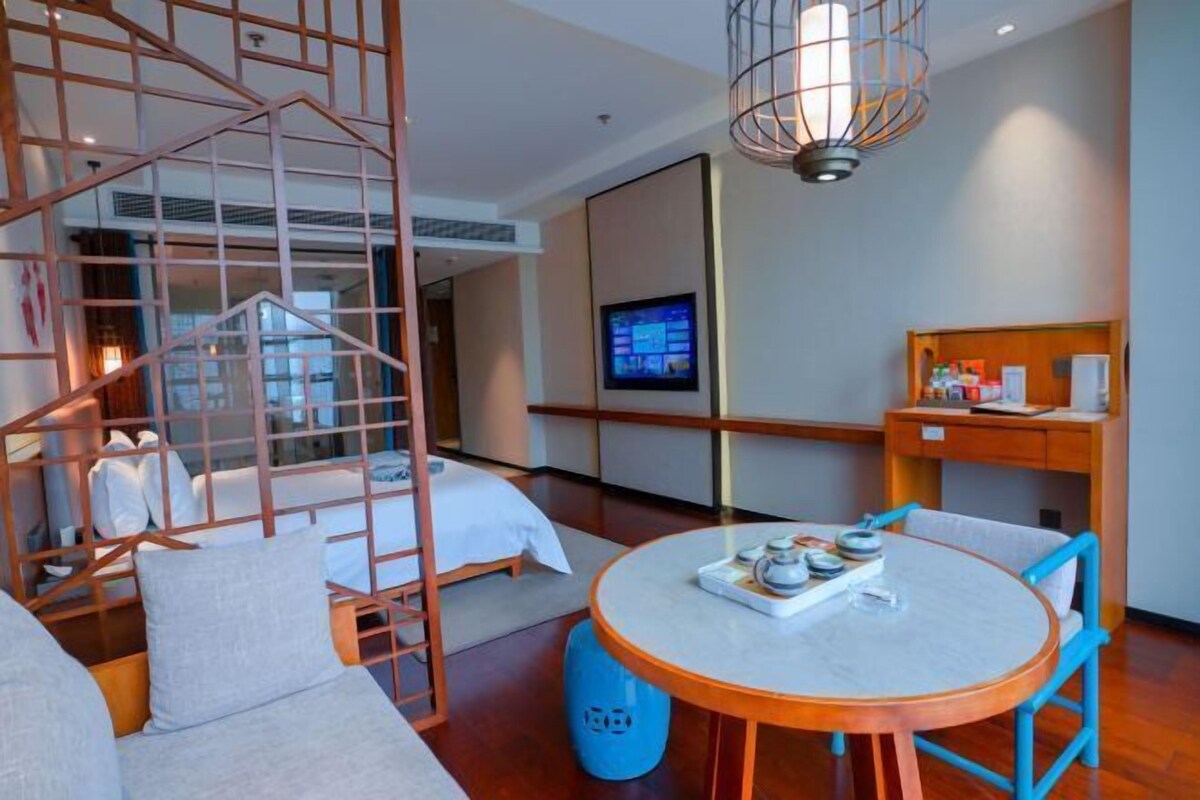 A modern hotel room with a bed, a small table with a tray of items, a TV, and a unique wooden structure in the corner.