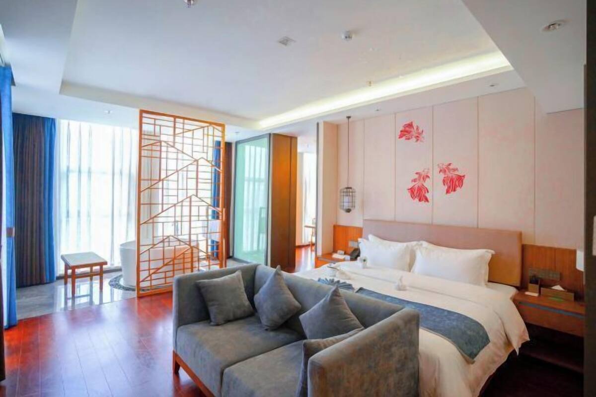 Habitación de hotel moderna con una cama grande, un sofá, un panel de madera y vistas al exterior.