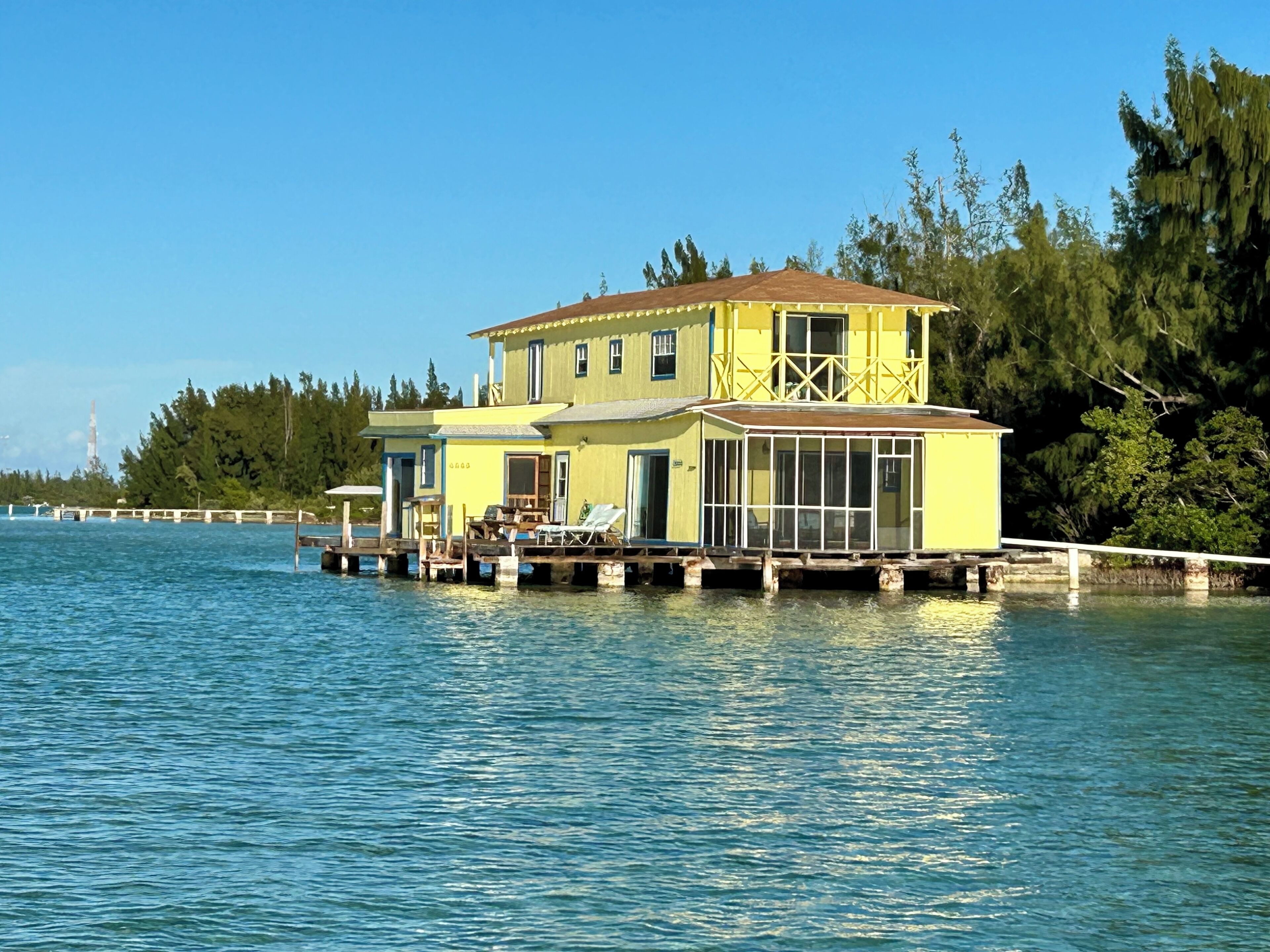 A two-story houseboat with a deck and a covered area, situated on a calm body of water.