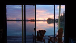 A view from a window overlooking a calm lake at dusk with two wooden chairs on a wooden deck. - Sunset Point Houseboat, a gem of a place (Fresh Creek)