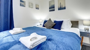 A hotel room with a neatly made bed, a bedside table with a lamp, and wall art. - 56HRC 5 BedRoom House| Garden| Parking PFP (Coventry)