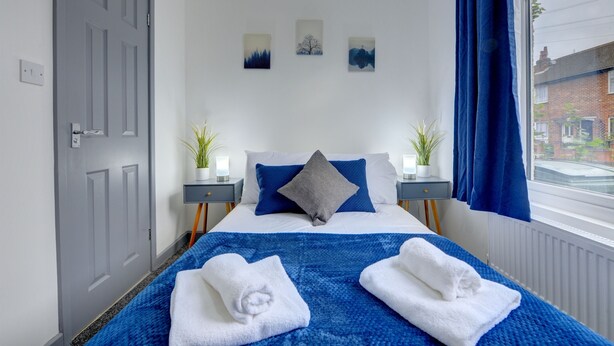 A neatly arranged bedroom with a bed, two bedside tables, a window with curtains, and a door. - 56HRC 5 BedRoom House| Garden| Parking PFP (Coventry)