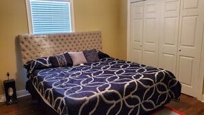 Une chambre à coucher avec une tête de lit capitonnée, une couvre-lit à motifs et une armoire blanche à deux portes.