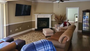 Un salon avec une cheminée, un téléviseur, un ventilateur de plafond et un grand miroir.