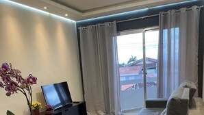 Uma sala de estar moderna com uma mesa de jantar de madeira, um sofá, uma TV e uma varanda com cortinas.