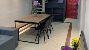 Um interior moderno com mesa de jantar de madeira, cadeiras pretas, sofá cinza, escada em espiral e uma porta vermelha.