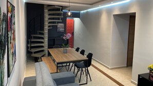 Uma área de refeições moderna com uma mesa de madeira, assentos acolchoados azuis e uma escada em espiral ao fundo.